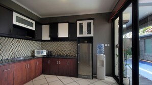 A modern kitchen with dark wood cabinets, a stainless steel refrigerator, and a tiled backsplash. - Jayani Villa (Seminyak)