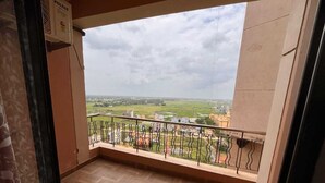 A balcony with a view of a cityscape, a tiled floor, and a wall-mounted air conditioner.