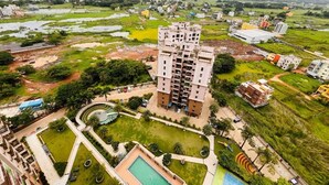 A high-rise building with multiple balconies, surrounded by green lawns and a swimming pool.