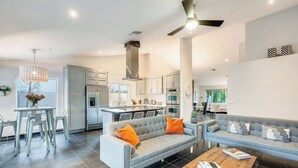 A modern kitchen with grey cabinets, a central island, and a dining area with a grey sofa and coffee table. - Meadow Hills in North Scottsdale / Heated Pool (Scottsdale)