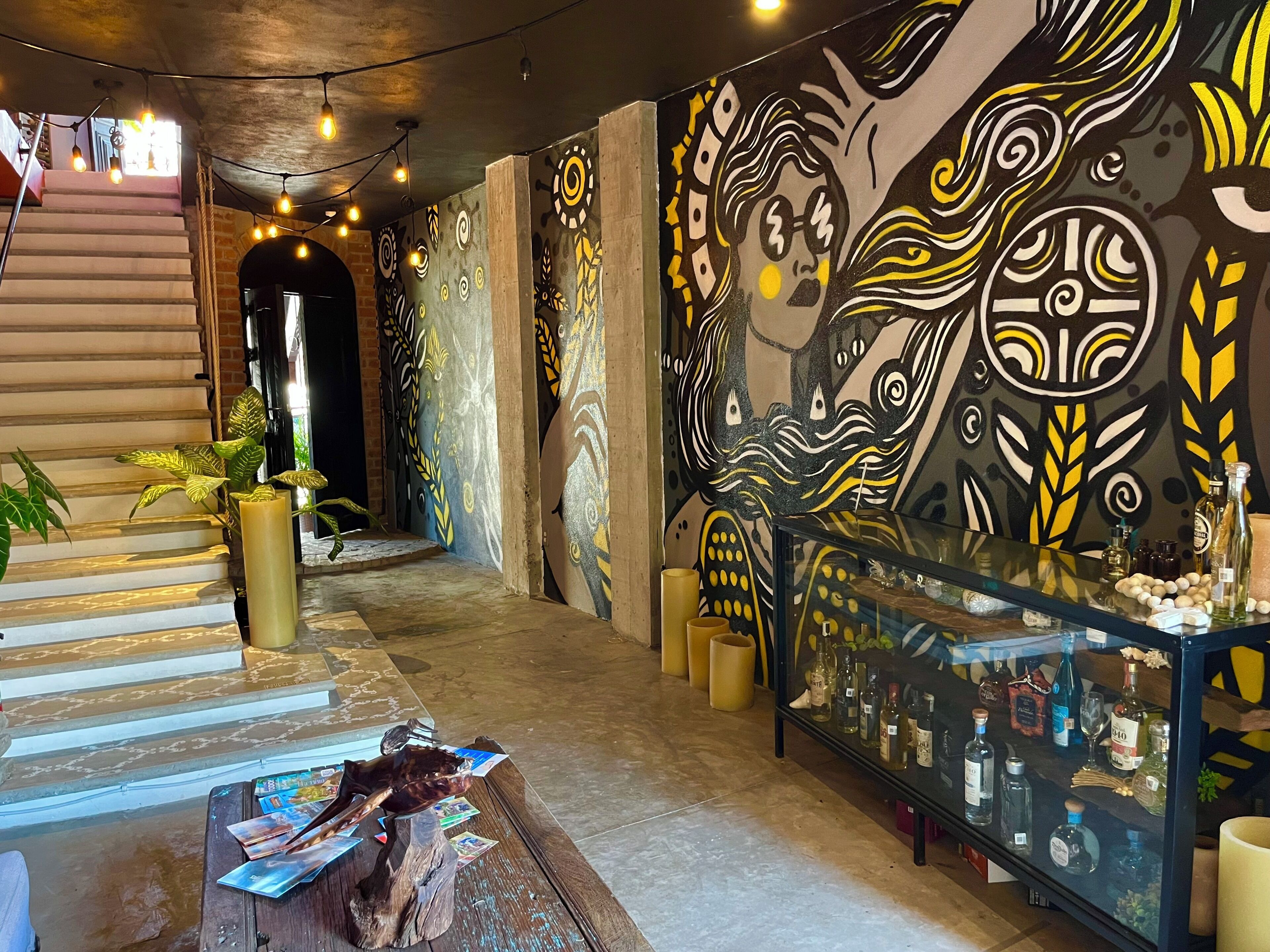 Un hall d’entrée avec un escalier, une vitrine contenant des bouteilles et une fresque murale.