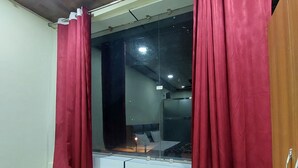 Ein Zimmer mit einem Bett, einem Fenster mit roten Vorhängen und Blick auf eine Stadtansicht.