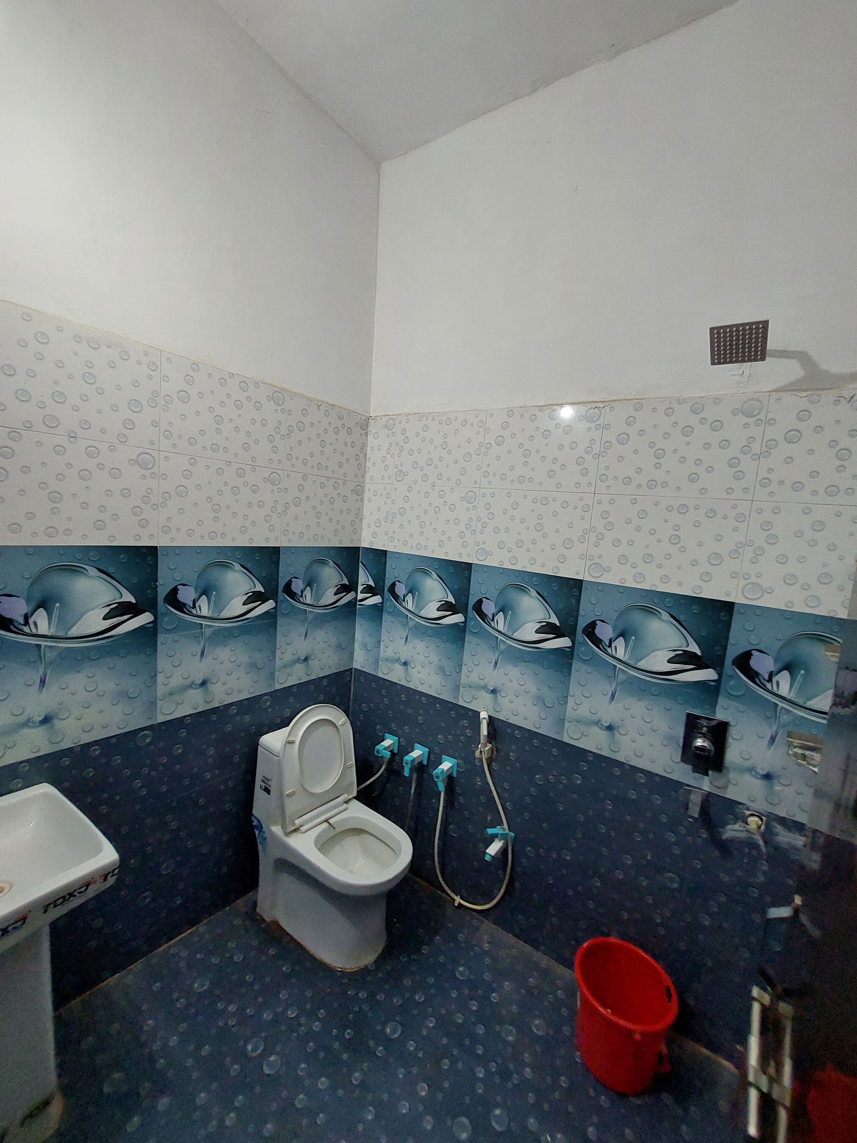 Een badkamer met een toilet, bidet en een rode emmer.