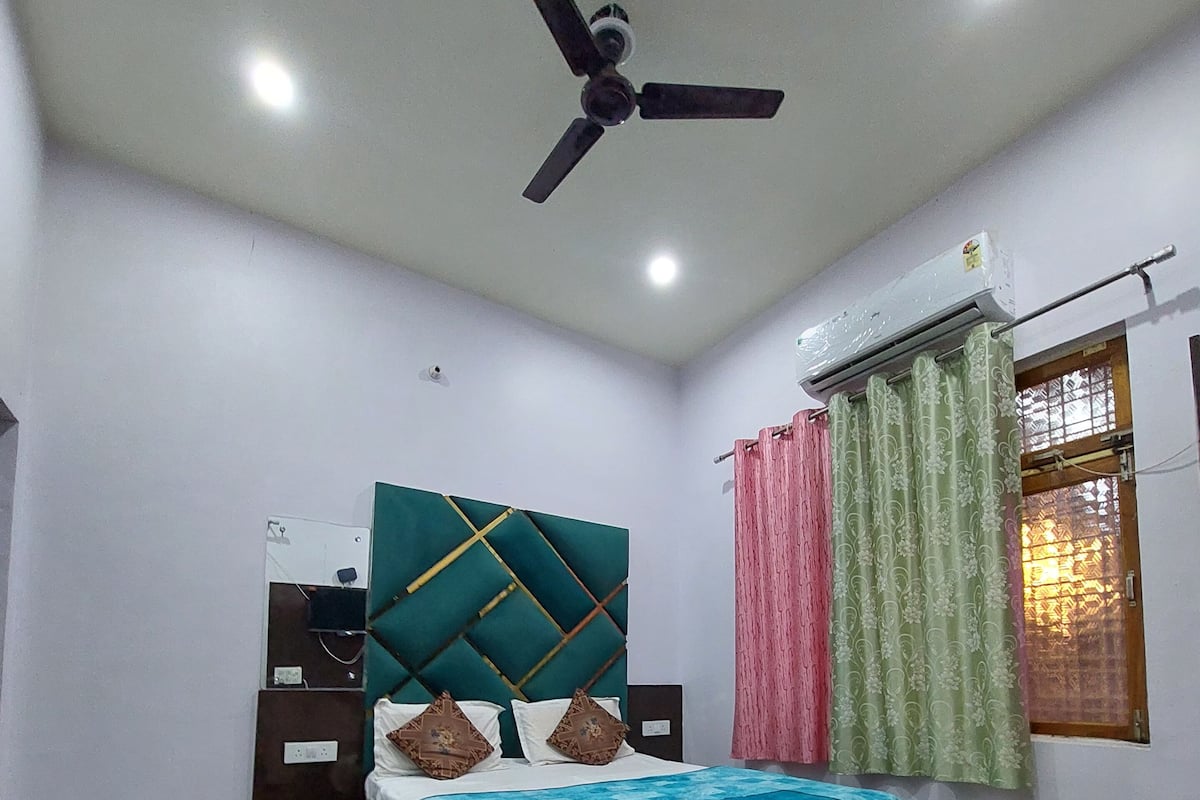 Un dormitorio con cama, ventilador de techo, ventana con cortinas y una silla verde.