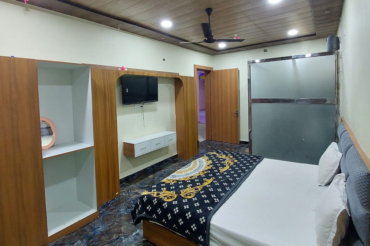 Un dormitorio con cama, televisión montada en la pared, ventilador de techo y suelo de mármol.