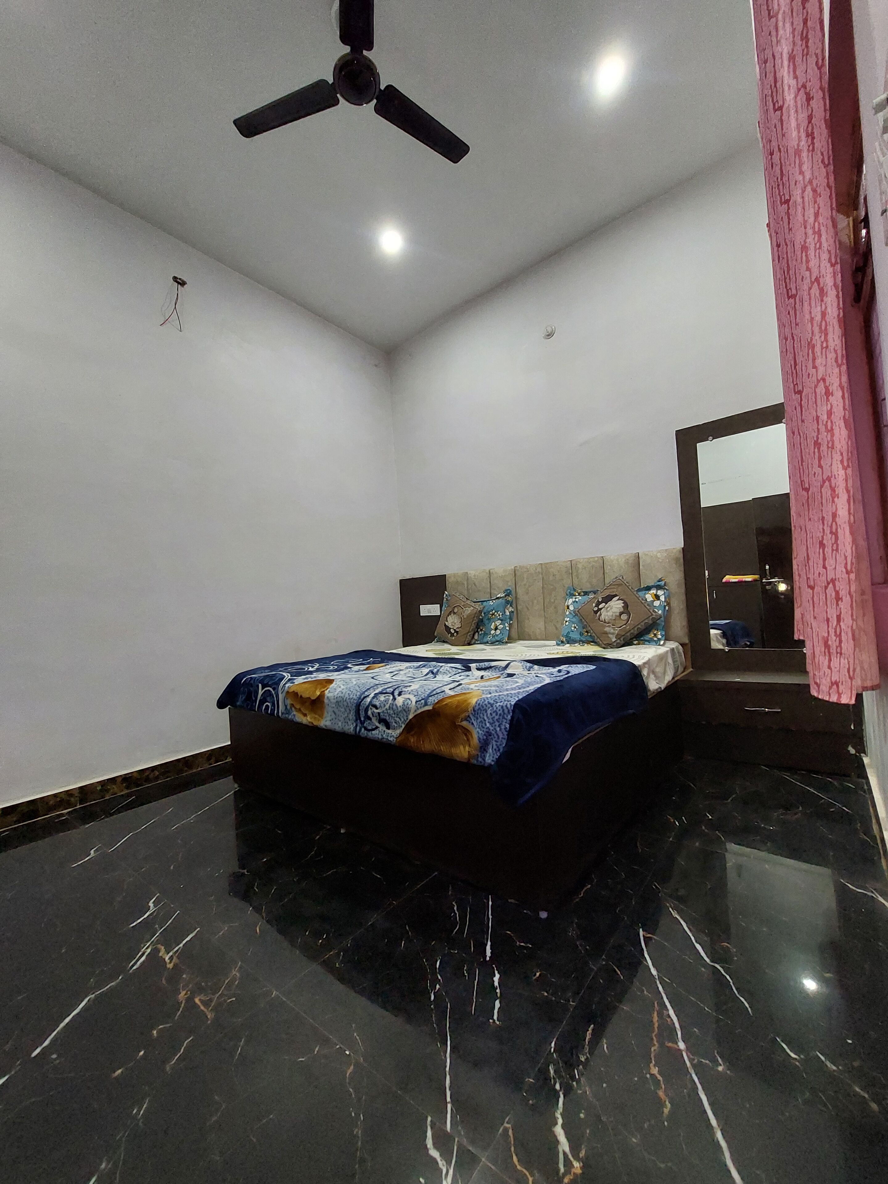 A bedroom with a bed, a ceiling fan, a mirror, and a pink curtain.