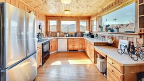 Cozinha moderna com armários de madeira, eletrodomésticos de aço inoxidável e grandes janelas com vista para as montanhas.