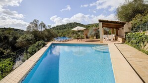 Ein Schwimmbecken mit Liegestühlen, einer Pergola und Blick auf eine hügelige Landschaft.