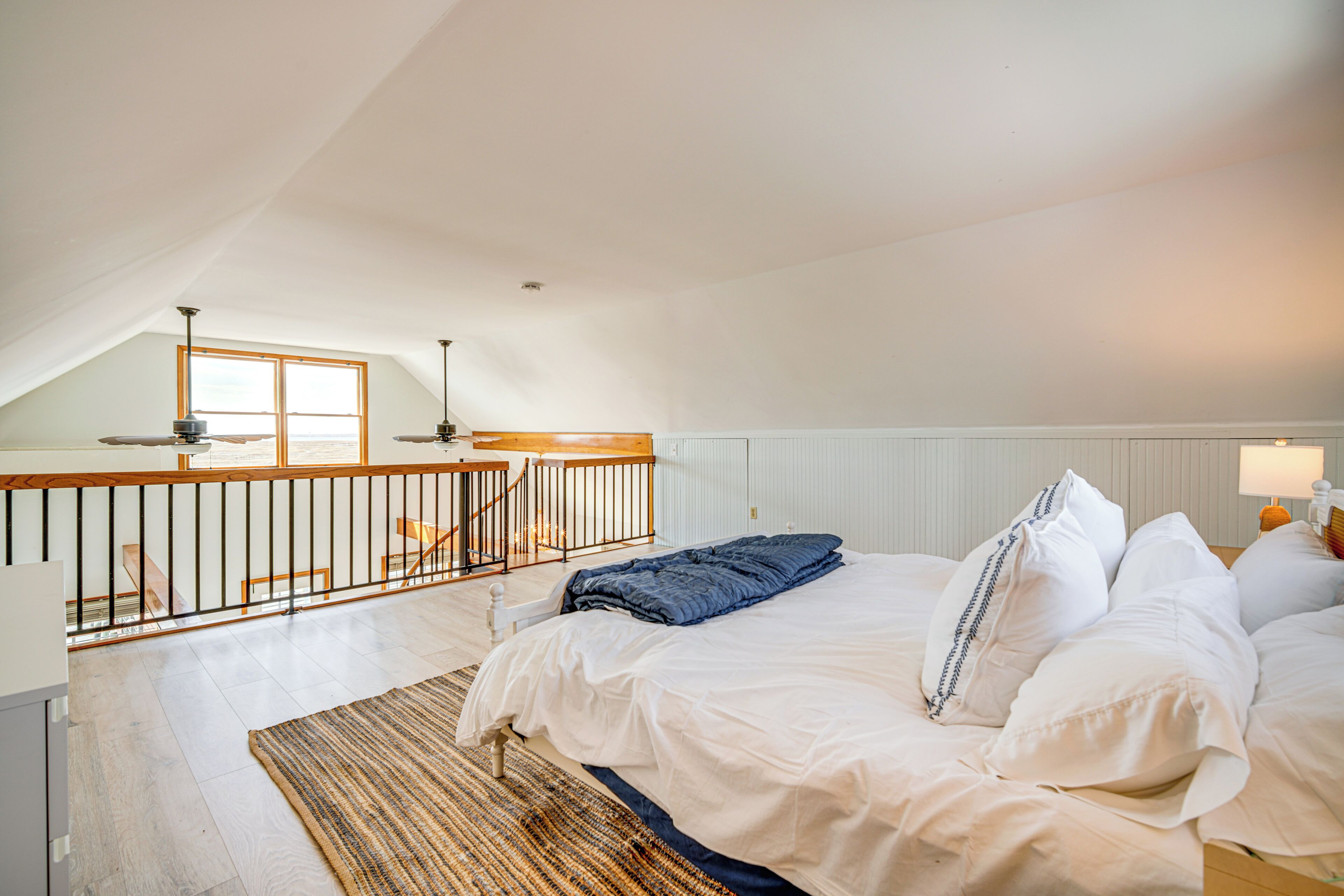 A bedroom with a large bed, a wooden railing, and a view of the outdoors.