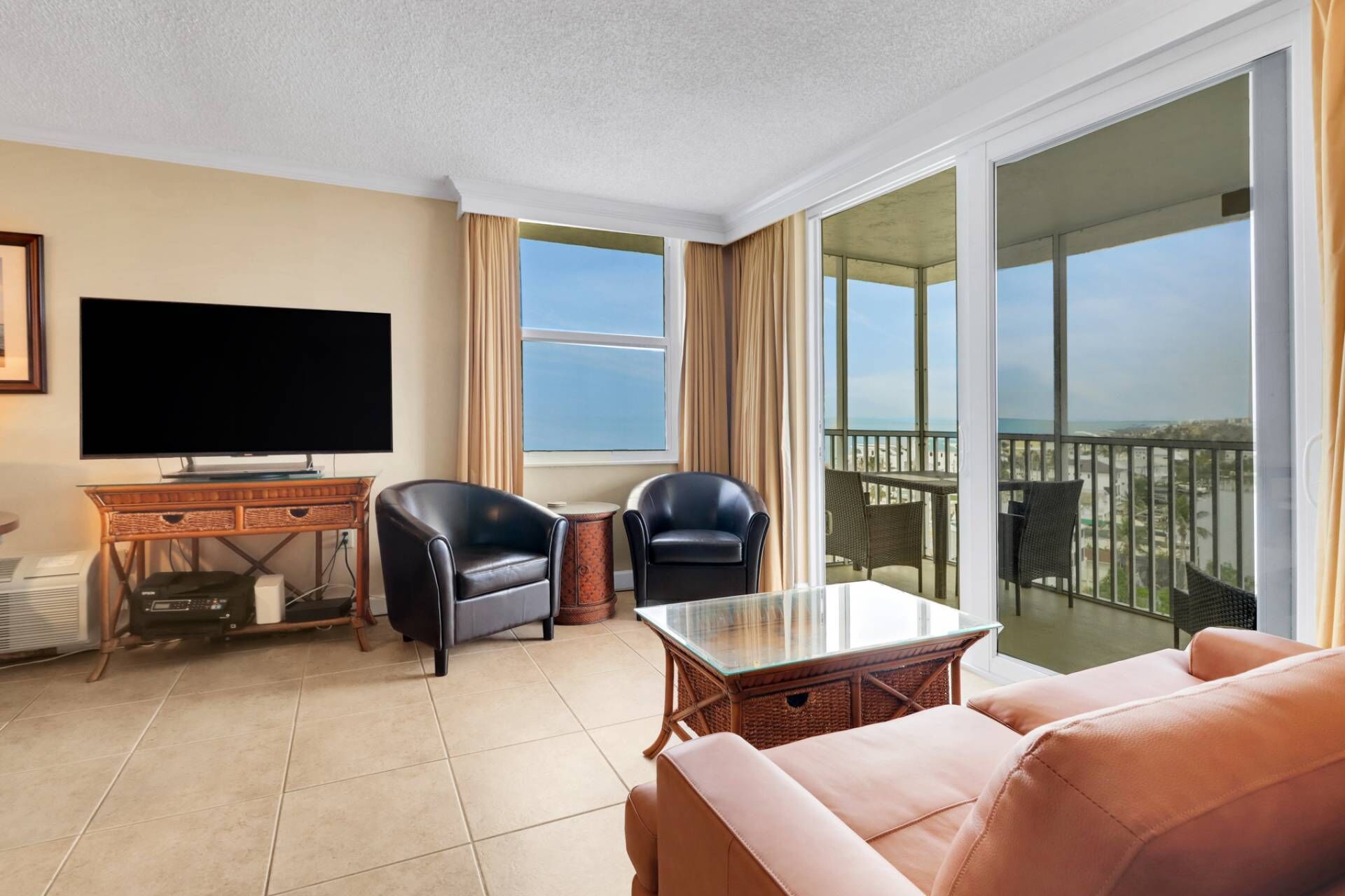 Een hotelkamer met een flatscreen televisie, twee leren fauteuils, een salontafel met glazen blad en een balkon met uitzicht op de stad.