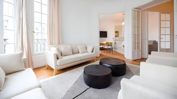 Ein modernes Wohnzimmer mit einem weißen Sofa, schwarzen Hocker und einem Streifen Teppich.