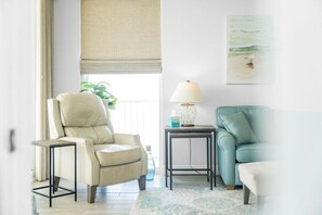 Un salon avec un fauteuil beige, un fauteuil turquoise, une petite table avec une lampe et un tableau accroché au mur.
