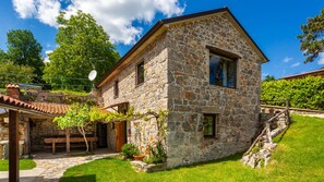 A stone house with a sloped roof, a wooden bench, and a stone pathway leading to the entrance.