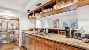 A modern kitchen with granite countertops, wooden cabinets, and a coffee station.