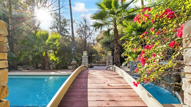 A wooden deck leading to a pool with stone walls and tropical plants.