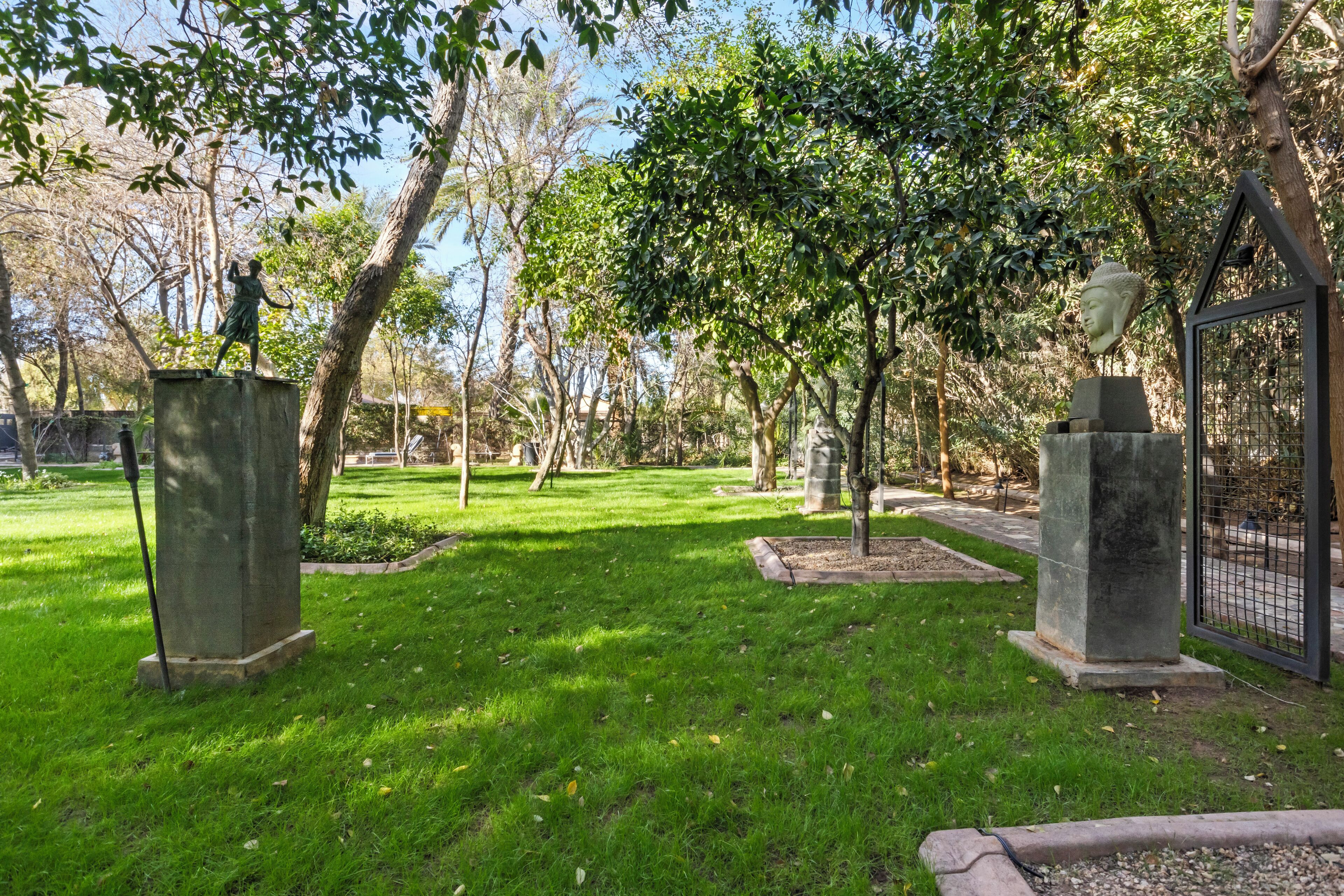 A park with statues, trees, and a fenced area.