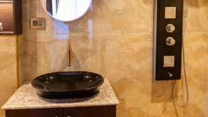 Casa de banho com espelho redondo, lavatório preto e chuveiro fixo na parede.