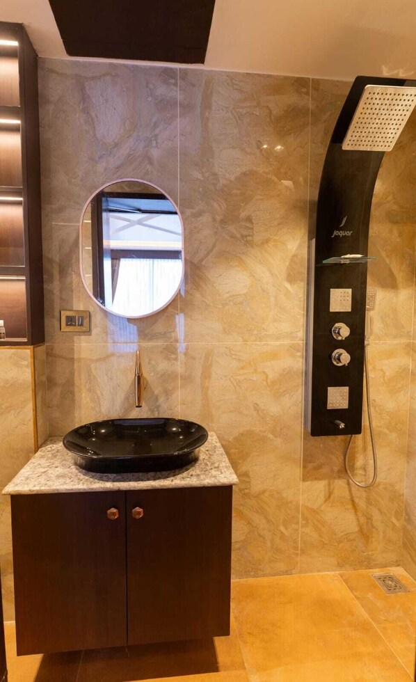 A bathroom with a round mirror, a black sink, and a wall-mounted shower. - Nachi Grand Residency (Devakottai)