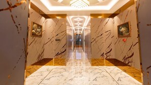 Corredor com paredes e pisos de mármore, que leva a uma área bem iluminada com design geométrico no teto.