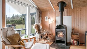 A cozy living room with a fireplace, wooden walls, and a large window overlooking a garden.