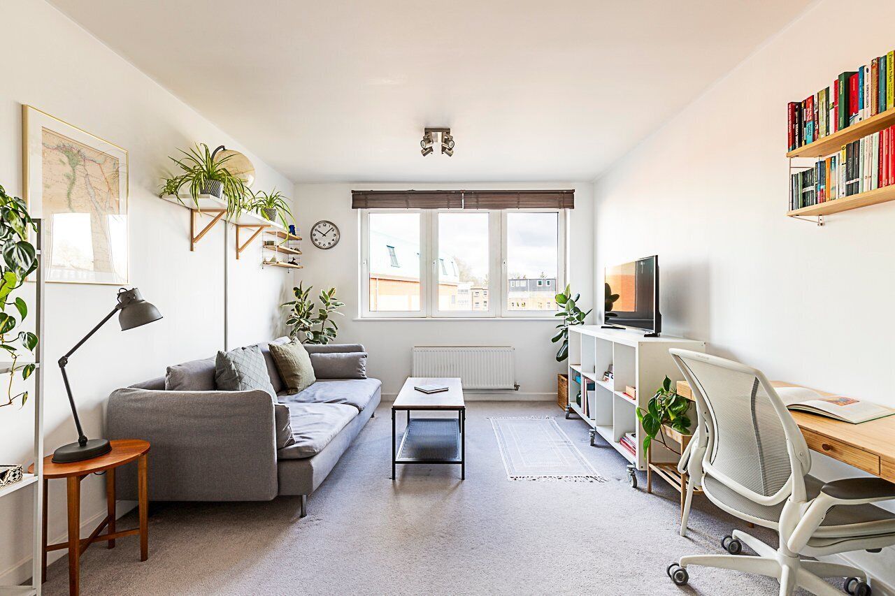 A modern living room with a grey sofa, a coffee table, a desk with a computer, and a bookshelf.