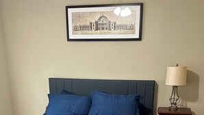 A bedroom with a large bed, a nightstand with a lamp, a framed picture on the wall, and a ceiling fan. - The Monroe: 2-bedroom townhome. Walk to LSU (Baton Rouge)