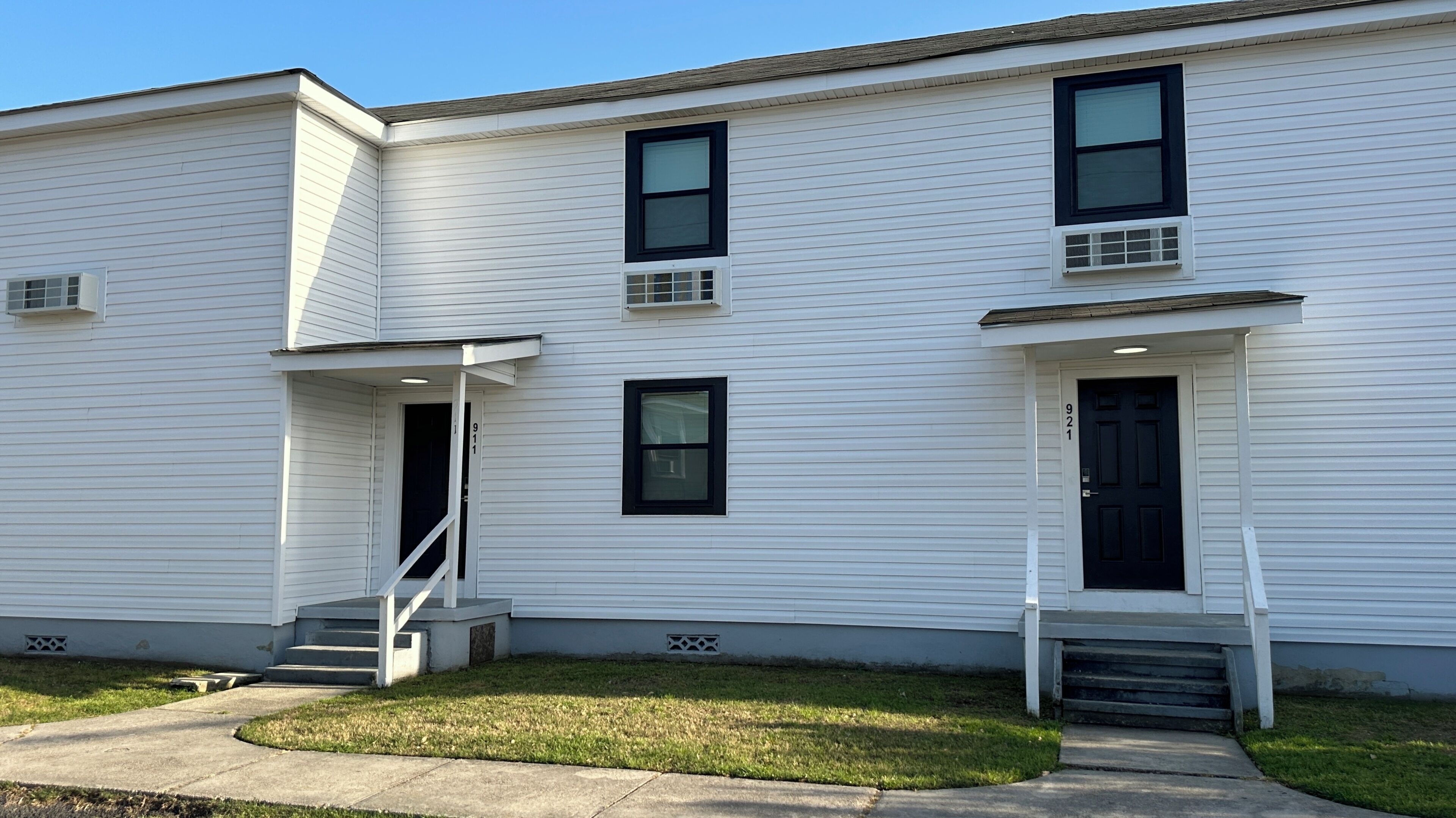 A two-story white building with a front porch, a staircase, and a small front yard.