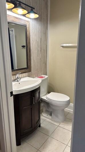 A bathroom with a white sink, dark wooden cabinets, a mirror with a decorative frame, and a toilet. - The Monroe: 2-bedroom townhome. Walk to LSU (Baton Rouge)