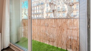 A sliding glass door leading to a balcony with a bamboo fence and a small patch of artificial grass.