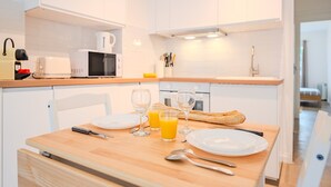 A modern kitchen with white cabinets, a wooden dining table set with plates, glasses, and cutlery, and a bread loaf.