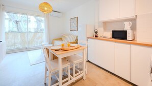 A bright kitchen with white cabinets, a microwave, and a coffee maker. There's a dining table with chairs and a hanging light fixture.