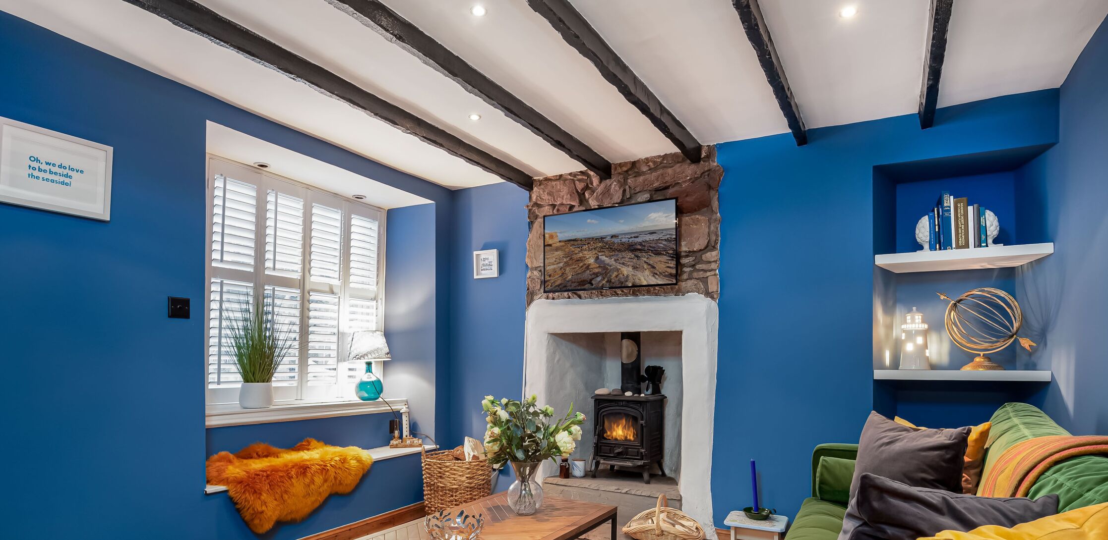 A cozy living room with a fireplace, a window with shutters, and a bookshelf.