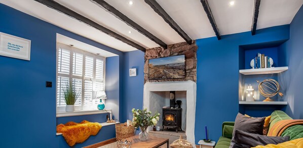 A cozy living room with a fireplace, a window with shutters, and a bookshelf. - Honeybee Cottage | Cellardyke (Cellardyke)