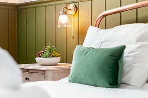 A neatly made bed with white and green pillows, a bedside table with a plant, and a wall-mounted lamp. - Honeybee Cottage | Cellardyke (Cellardyke)