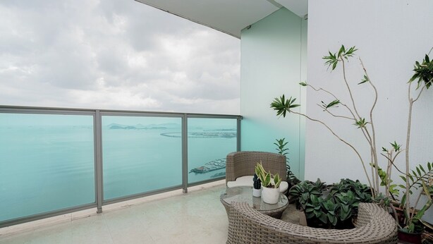A balcony with a view of the sea, wicker furniture, and potted plants.