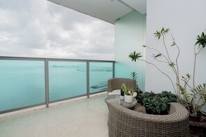 Een balkon met uitzicht op zee, rieten meubilair en potplanten.