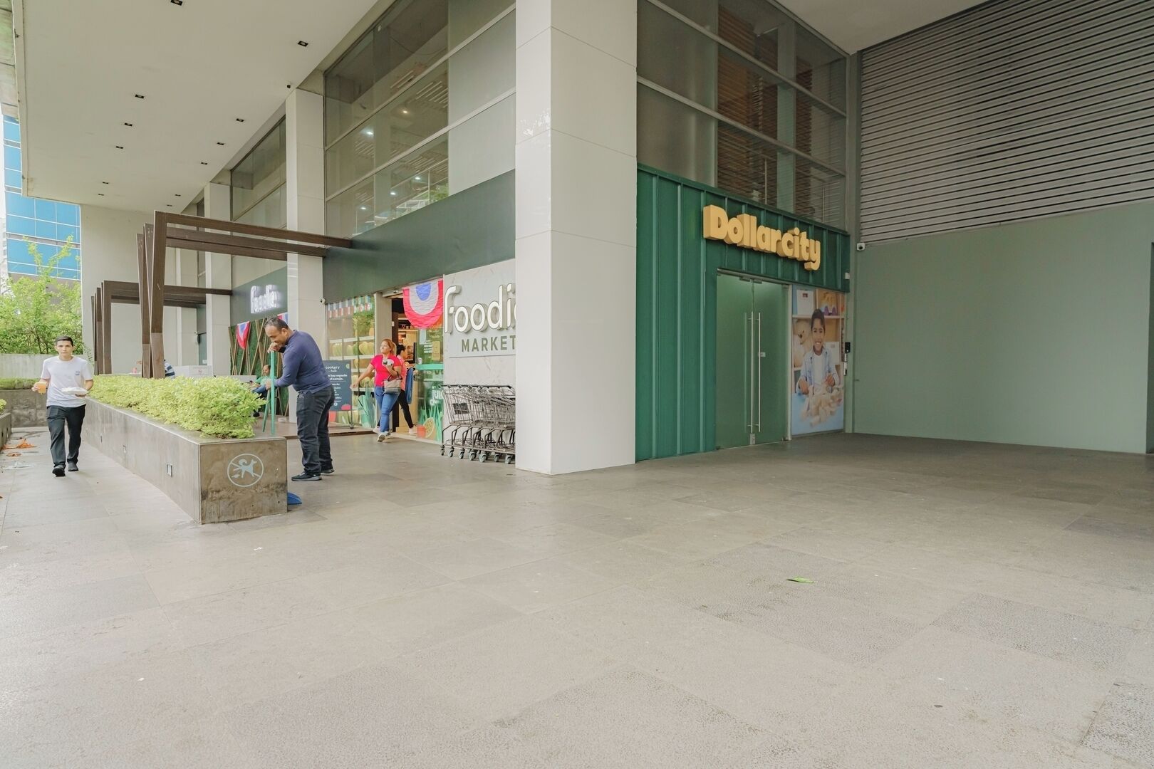 Un edificio moderno con una entrada amplia, un letrero visible que dice 'Dollarcity' y un letrero que indica 'Food Market'.