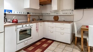 A compact kitchen with white cabinets, a red kettle, and a tiled floor. - 4-Studio Steinplatte (Reit im Winkl)