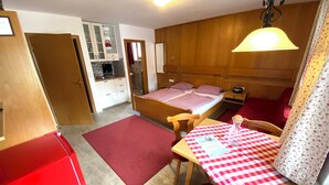 A compact room with a bed, a dining table with a checkered tablecloth, a red chair, a small kitchen area, and a red refrigerator. - 4-Studio Steinplatte (Reit im Winkl)