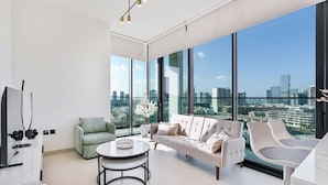Un salon moderne avec un canapé, des fauteuils et une table à manger. De grandes fenêtres offrent une vue sur la ville.