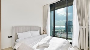 Une chambre d’hôtel moderne dotée d’un grand lit, d’une table de chevet et offrant une vue sur la ville grâce à de grandes fenêtres du sol au plafond.