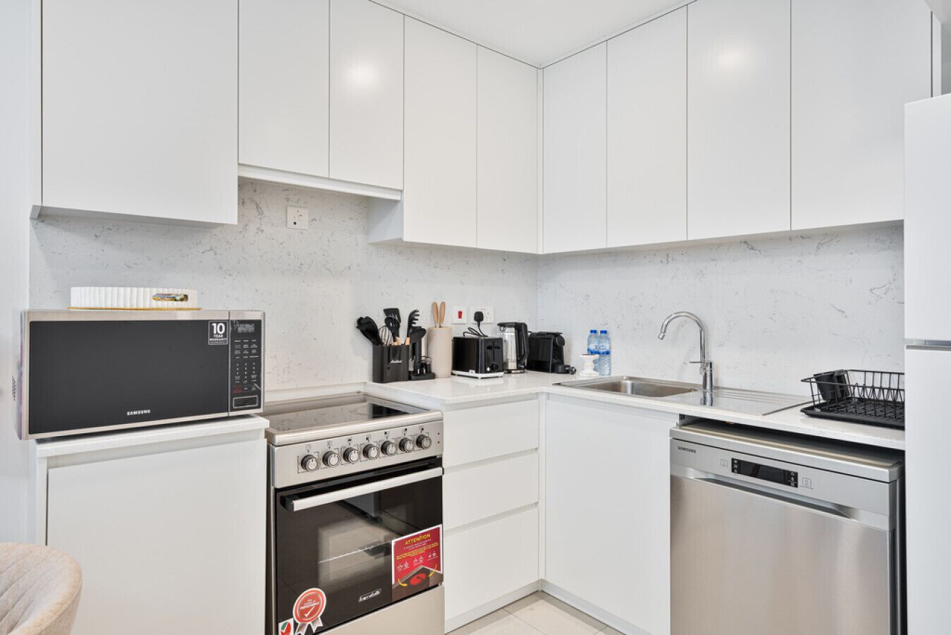 Une cuisine moderne avec des meubles blancs, un four à micro-ondes, une cuisinière, un four, un lave-vaisselle et un évier.