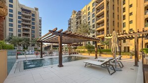 A rooftop pool area with sun loungers and a pergola, surrounded by high-rise buildings.