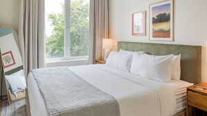 Cama bem arrumada com lençóis brancos, cabeceira e mesa de cabeceira com abajur.