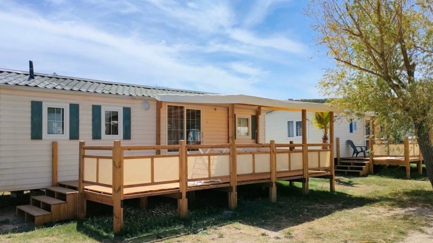 Una casa móvil con terraza de madera, un porche cubierto y una pequeña zona de estar al aire libre.
