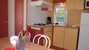 A compact kitchen with a gas stove, sink, and a window. There is a dining table with chairs and a vase of flowers.