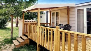 Eine Holzterrasse mit überdachter Sitzgelegenheit, einer Schiebetür aus Glas und einer kleinen Außenküche.