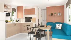Un espace de vie compact comprenant un coin cuisine, un coin repas et un canapé agrémenté d’un coussin décoratif.