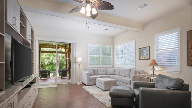 A modern living room with a sectional sofa, a flat-screen TV, and a ceiling fan. - Fairways at Mauna Lani Unit 1405 Garden View 3 Bed (Waimea)