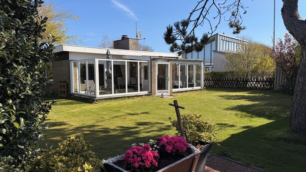 Ein modernes Haus mit großen Glasfenstern, einem gepflegten Rasen und einer Satellitenschüssel.